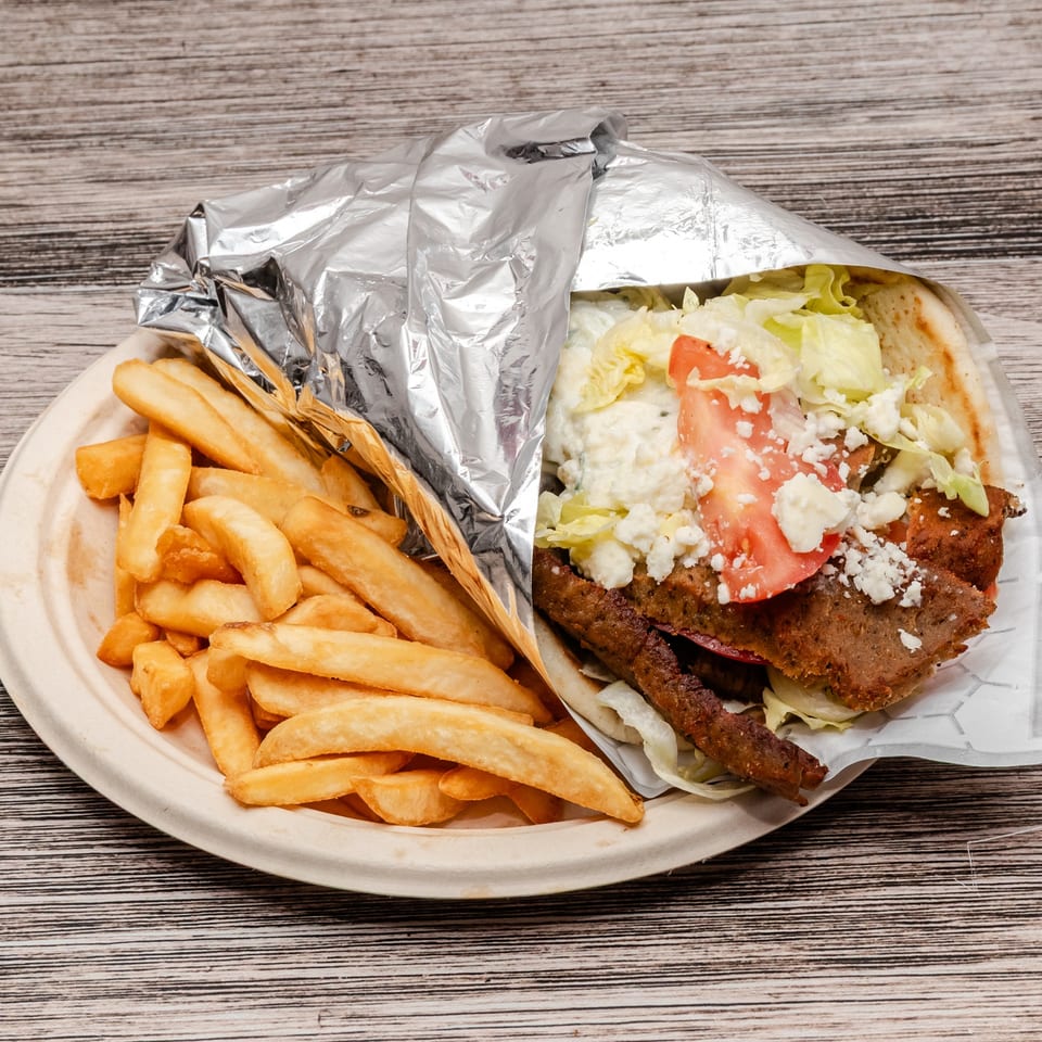 Gyro pita sandwich with lettuce, tomato, and feta beside golden fries on a plate.