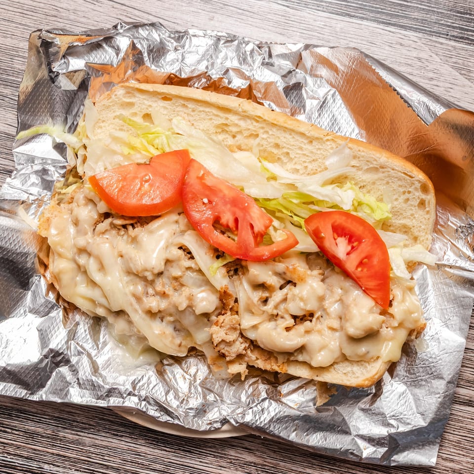 Loaded toasted sandwich with melted cheese, lettuce, tomato, and creamy filling wrapped in foil on a wood-grain table.