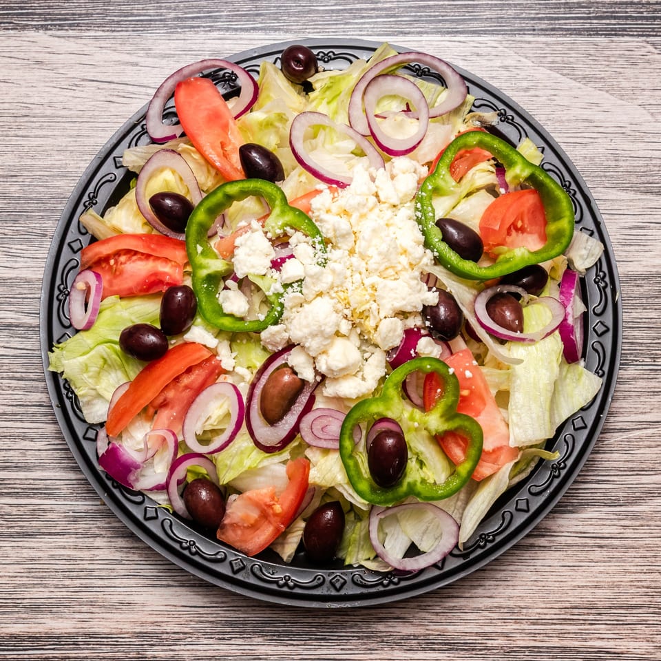 Greek salad with lettuce, tomatoes, red onions, green peppers, olives, and crumbled feta on a decorative plate.